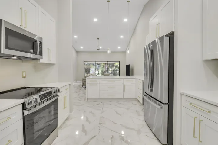 Contemporary kitchen featuring stainless steel appliances, white cabinetry with gold-tone hardware, and light-toned, veined tile flooring
