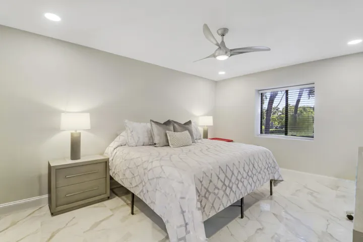 Recessed ceiling lighting, modern ceiling fan, large window with blinds, light-toned walls, and marble-look tile flooring