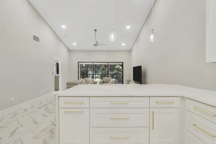 White cabinetry with gold-tone hardware, white countertop, and marble-look flooring