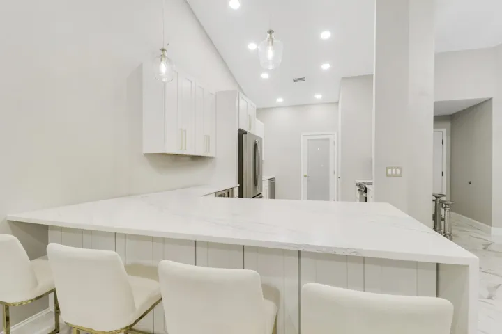 U-shaped kitchen island with white countertop, white cabinetry with gold-tone hardware, stainless steel appliances, and recessed lighting