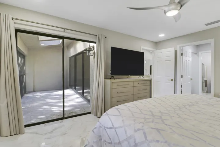 Sliding glass doors opening to a private patio, modern ceiling fan with integrated lighting, and white tile flooring
