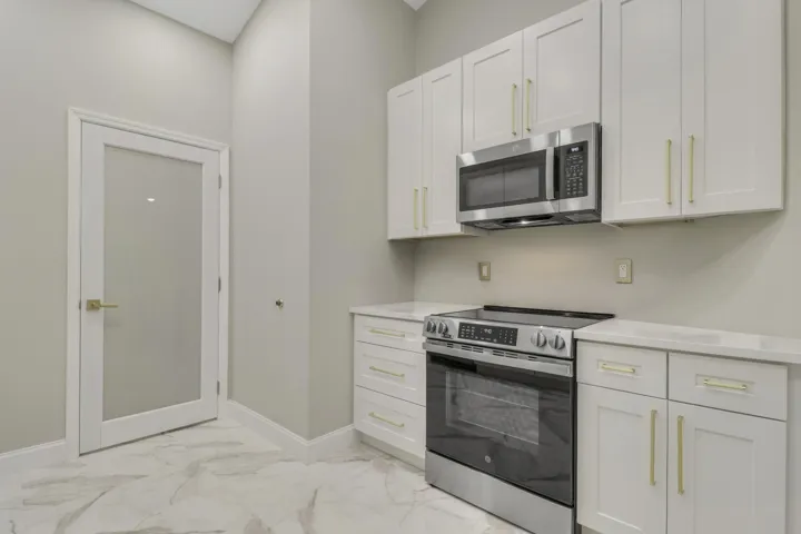 Kitchenette with white shaker cabinetry, stainless steel appliances, light-colored countertops, and marble-look flooring