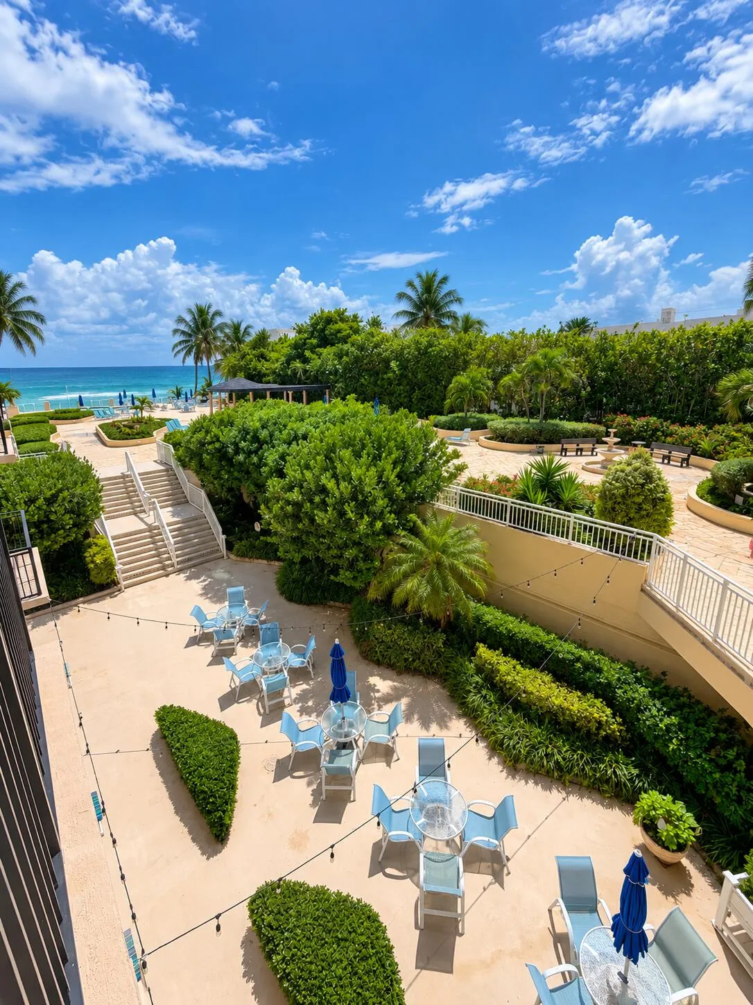 Expansive outdoor patio with multiple seating areas, lush landscaping, and stone staircases