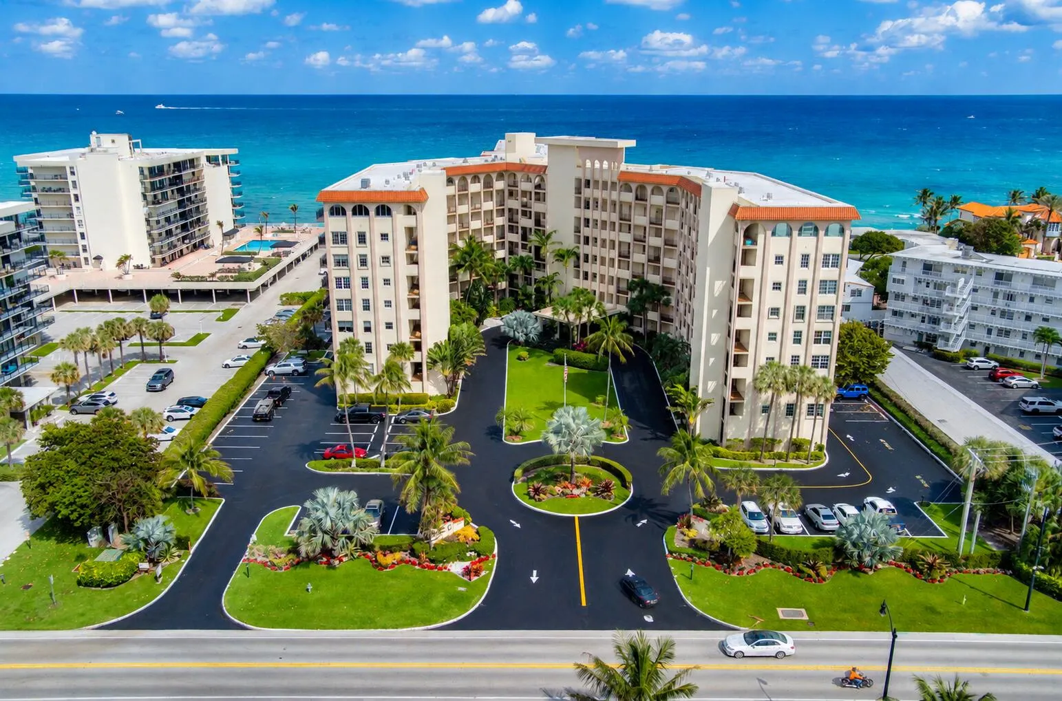 Coastal multi-story building featuring multiple balconies, a circular driveway, and landscaped grounds