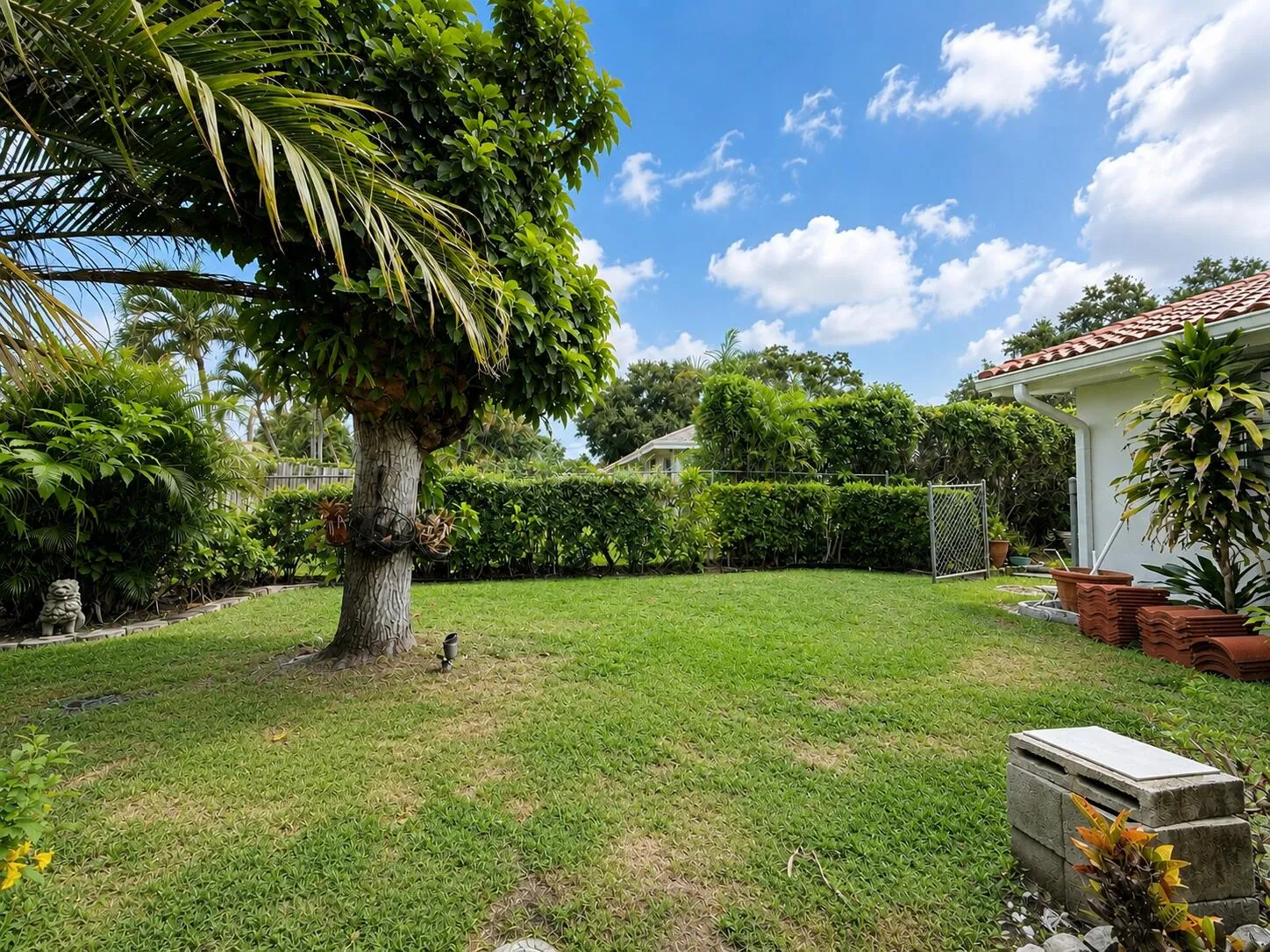 Manicured lawn, mature trees, dense privacy hedge, and a tile-roofed structure