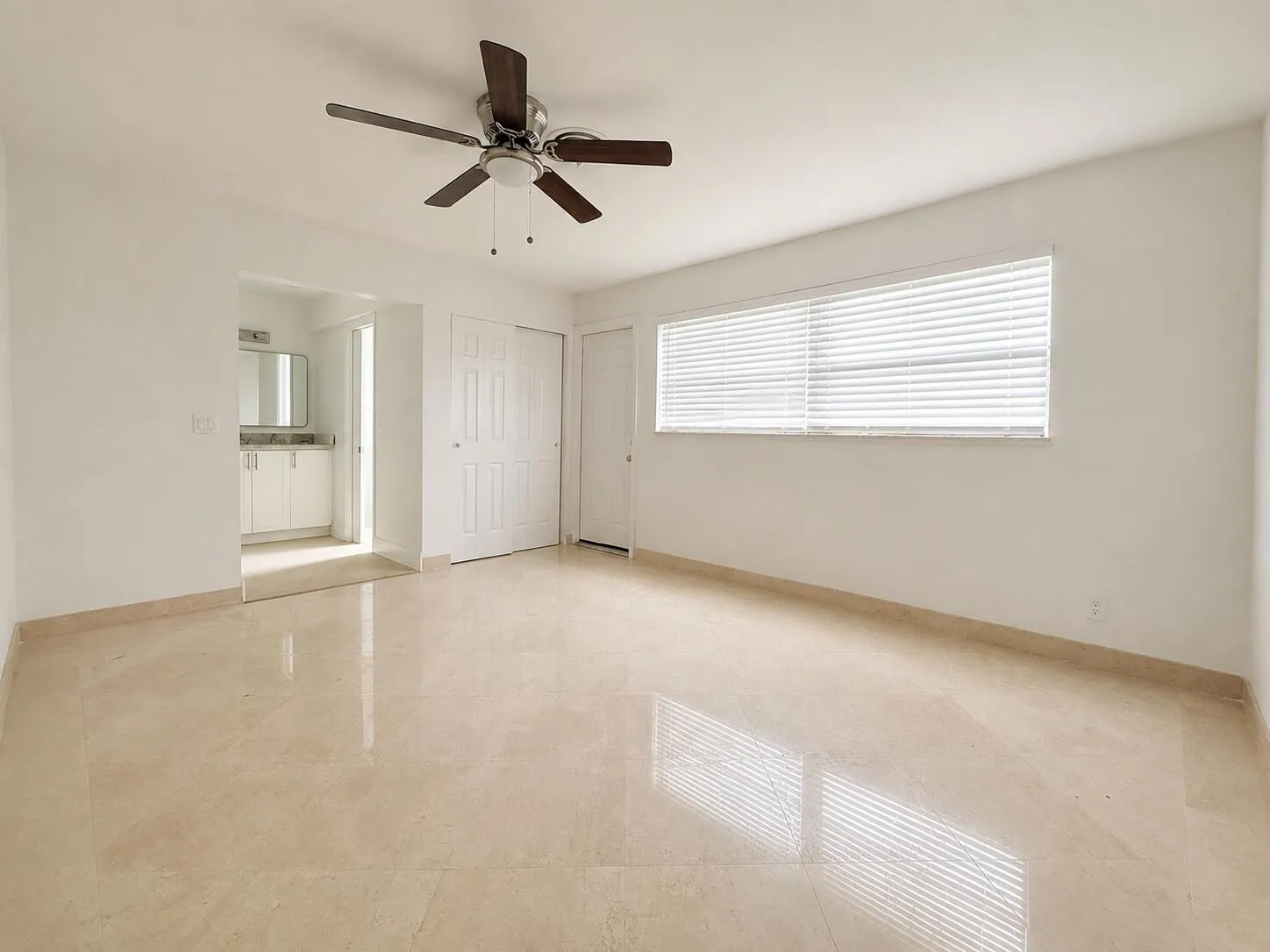 Spacious room featuring light-toned tile flooring, a ceiling fan with integrated lighting, and horizontal blinds on a large window