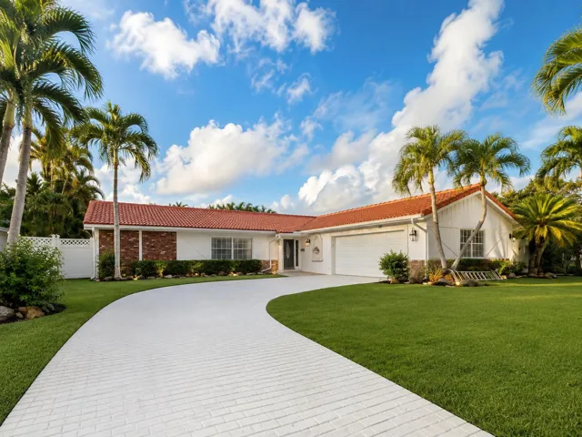 Curved paver driveway leading to a residence with a red tile roof, white exterior, and brick facade accents