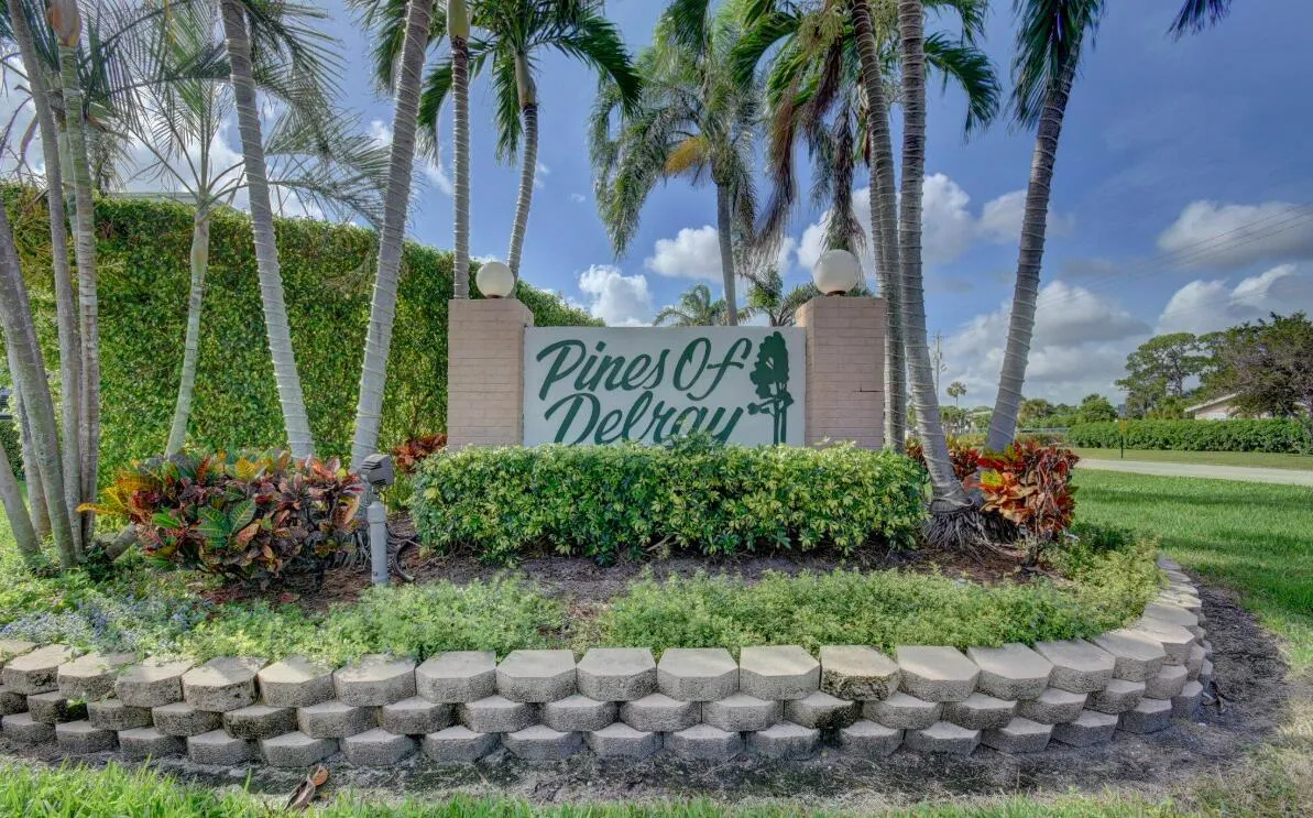 Community entrance sign featuring stacked stone landscaping, mature palm trees, and lush greenery