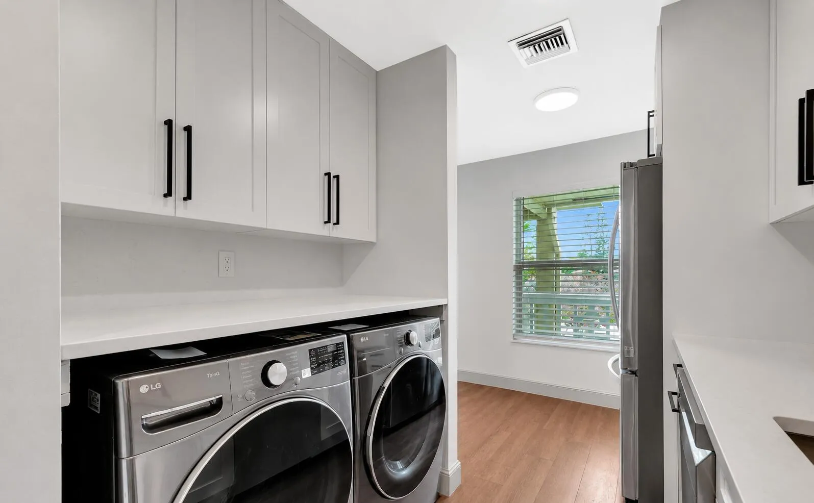 Laundry area with light-toned cabinetry, matte black hardware, and an expansive countertop