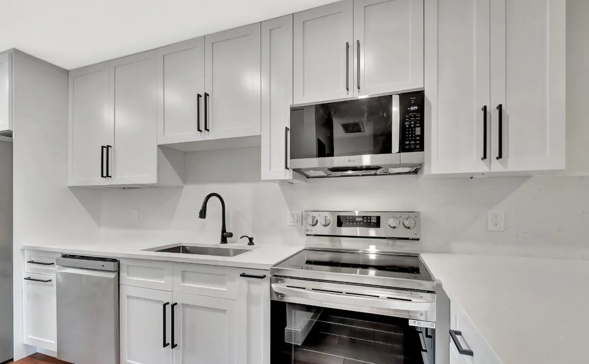 Modern kitchen featuring white shaker cabinetry, stainless steel appliances, a matte black faucet, and light-toned countertops