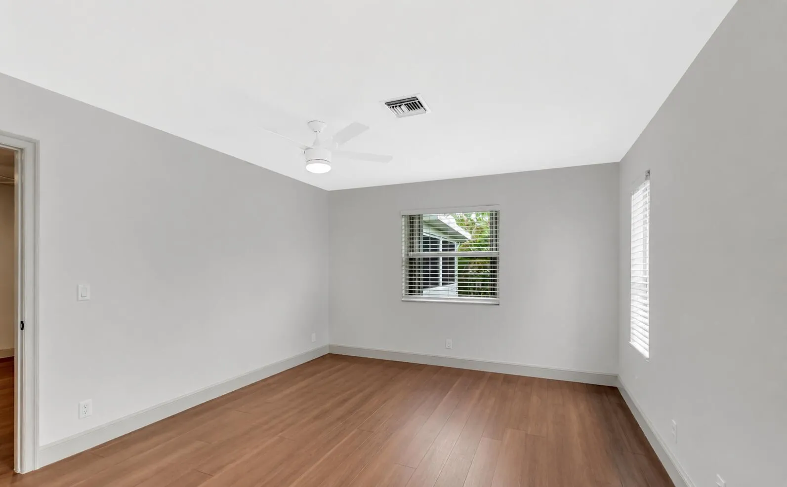 Wood-finish flooring, neutral wall tones, window treatments, and a ceiling fan with integrated lighting
