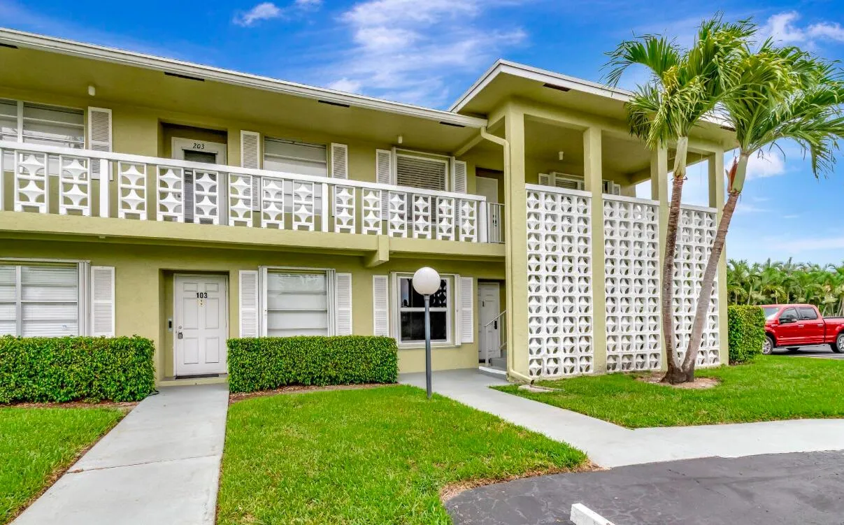 Multi-story exterior with stucco finish, decorative balcony railing, ground-level shrubbery, and mature palm trees