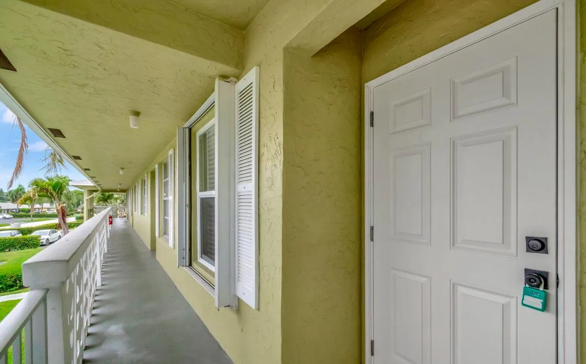 Textured exterior wall finish, paneled entry door, louvered window shutters, covered walkway, and decorative railing