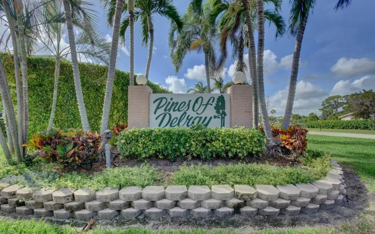 Community entrance sign featuring stacked stone landscaping, mature palm trees, and lush greenery