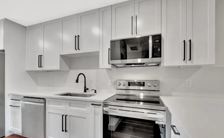 Modern kitchen featuring white shaker cabinetry, stainless steel appliances, a matte black faucet, and light-toned countertops