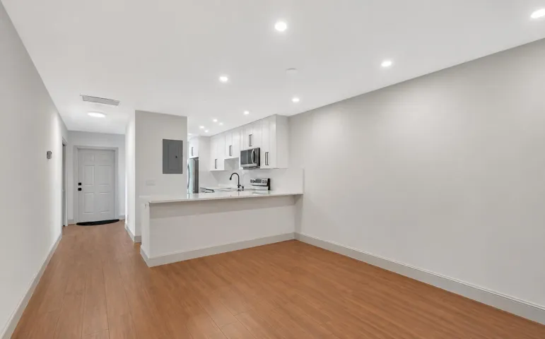 Open-concept living area with wood-finish flooring, recessed lighting, and a kitchen featuring white cabinetry, stainless steel appliances, and a breakfast bar