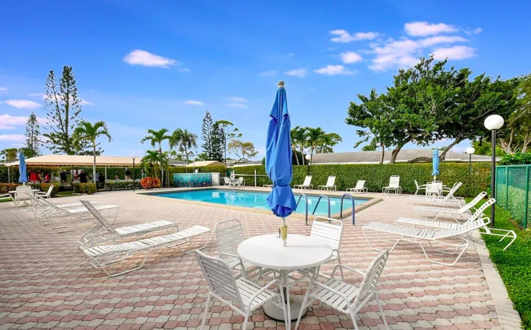 Outdoor swimming pool with a water feature, paver patio, mature landscaping, and an adjacent covered area