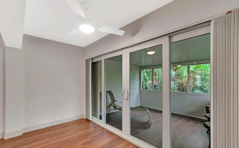 Sliding glass doors opening to an enclosed patio, wood-finish flooring, and a ceiling fan with integrated lighting