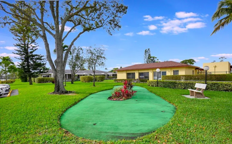 Manicured lawn with mature trees and shrubbery, featuring a putting green and a decorative island with vibrant plantings