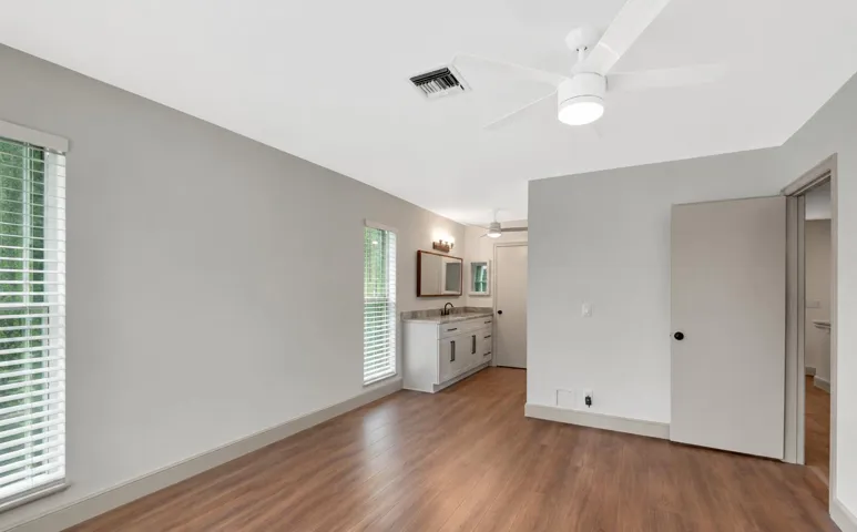 Wood-finish flooring, two windows with blinds, a modern ceiling fan, and a built-in vanity with a countertop and sink