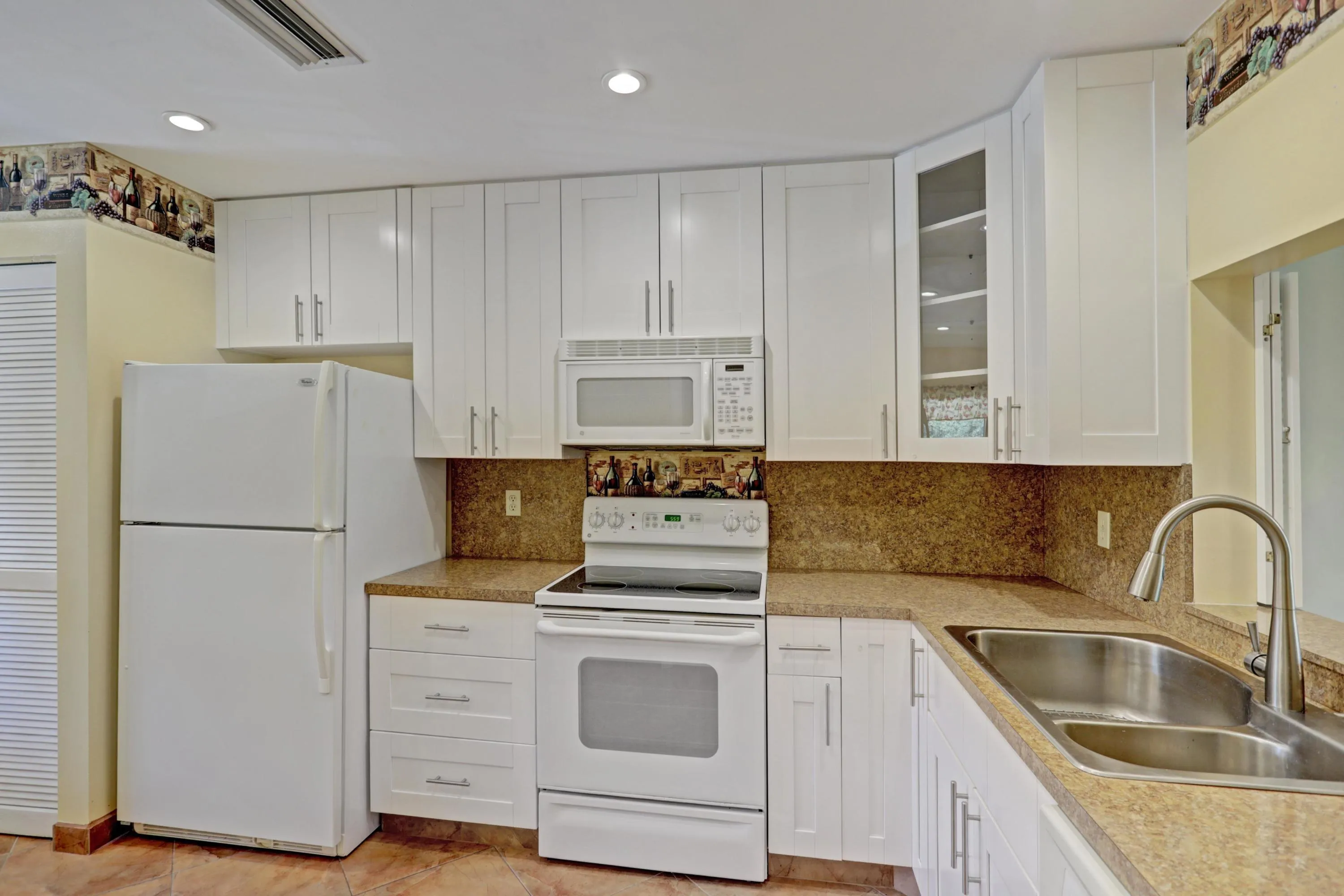 Kitchen featuring white cabinetry, a double basin stainless steel sink with a high-arc faucet, and integrated white appliances including a refrigerator, range, and microwave