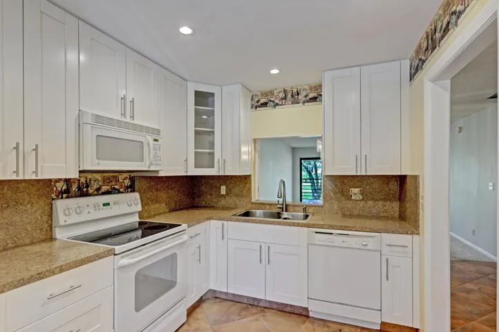 White cabinetry with brushed nickel hardware, speckled countertops, and coordinating backsplash