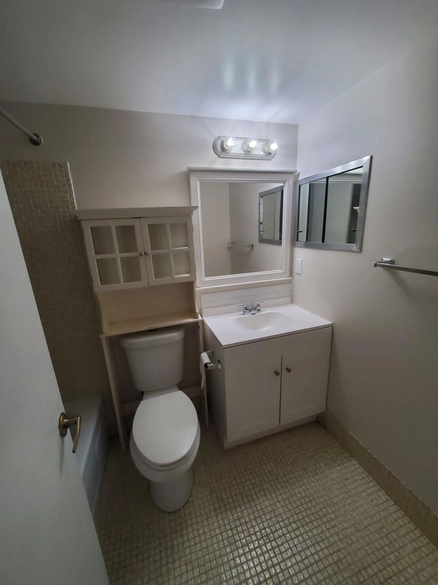 Bathtub with mosaic tile surround, shower fixture, and built-in toilet-side cabinetry