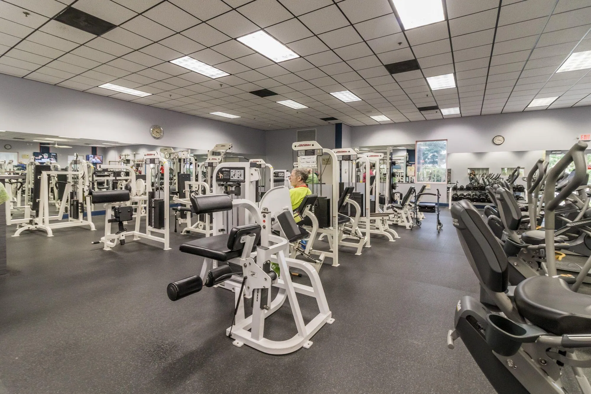 Spacious fitness center featuring rubber flooring, drop ceiling with integrated lighting, wall-mounted mirrors, and multiple exercise machines