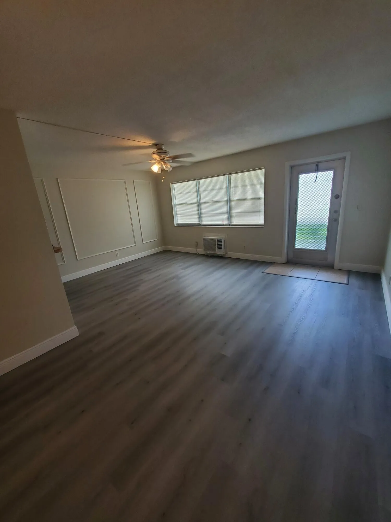 Livingroom featuring decorative wall molding, a ceiling fan with integrated lighting, wood-finish laminate flooring, and a pass-through opening to the Kitchen
