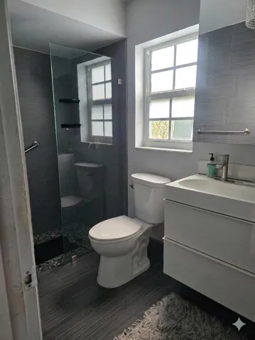 Modern bathroom featuring a glass-enclosed shower with dark pebble flooring, a wall-mounted vanity with an integrated sink, and dark wood-finish tile flooring