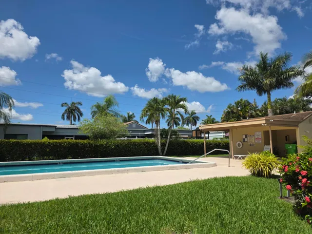 Community swimming pool with surrounding concrete decking, lush green lawn, tropical landscaping, and mature palm trees
