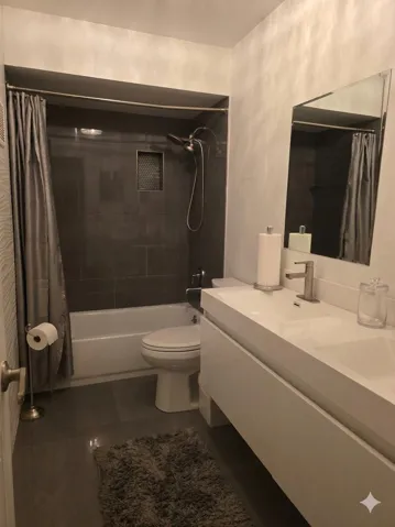 Floating vanity with integrated basin, brushed nickel faucet, large wall mirror, and floor-to-ceiling dark tile shower surround with niche