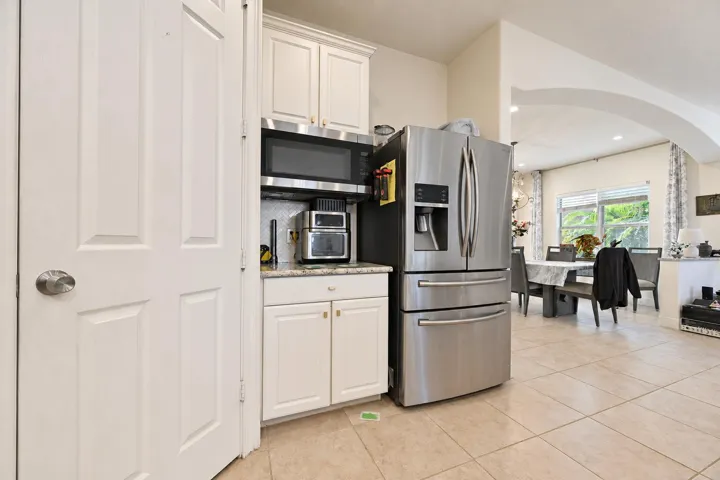 Stainless steel French door refrigerator, white upper and lower cabinetry, light-toned tile flooring, and an arched architectural opening