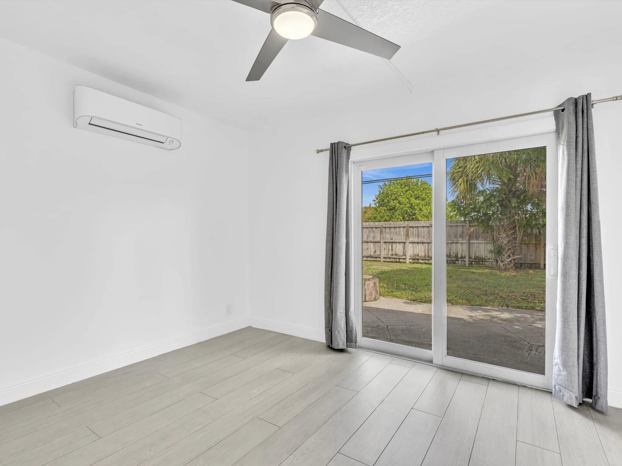 Bedroom with wood-finish ceiling fan with integrated lighting, and light grey vinyl flooring, sliding door exit to backyard