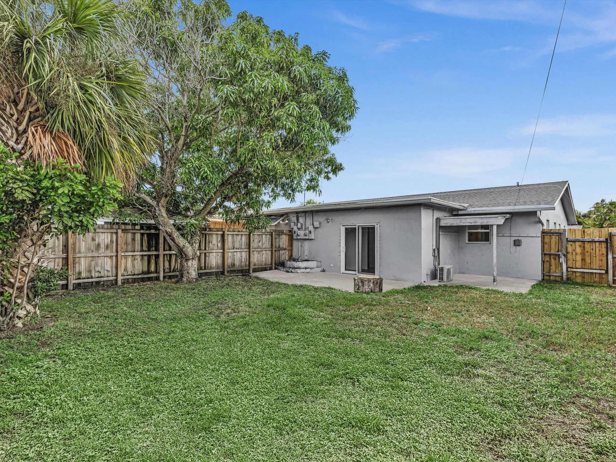 Private expansive fenced backyard featuring a concrete patio, wood fence, mature trees, and a grass lawn