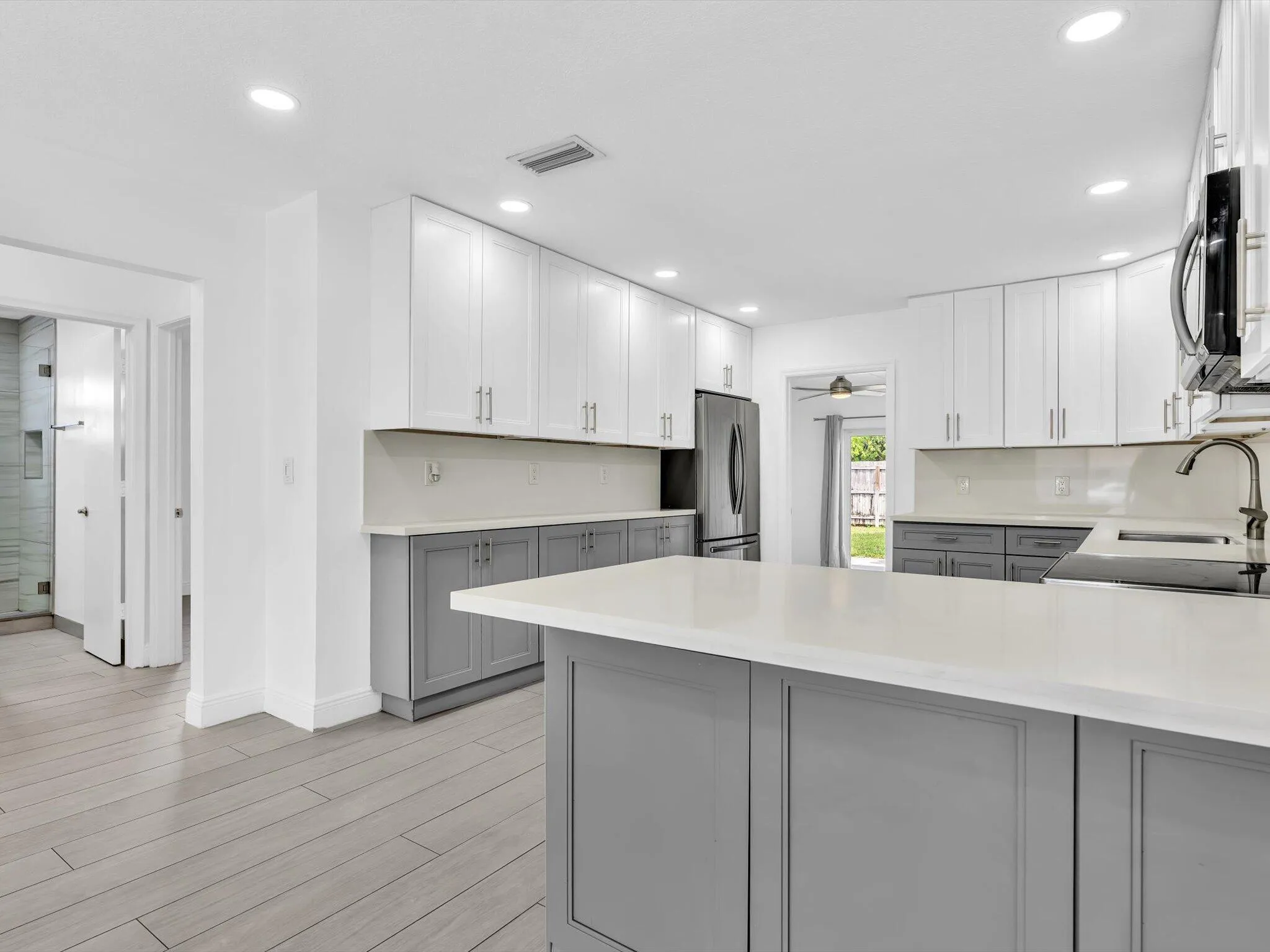 Kitchen featuring wood-finish vinyl flooring, two-tone cabinetry with white upper and grey lower units, stainless steel appliances, recessed lighting, and a white countertop