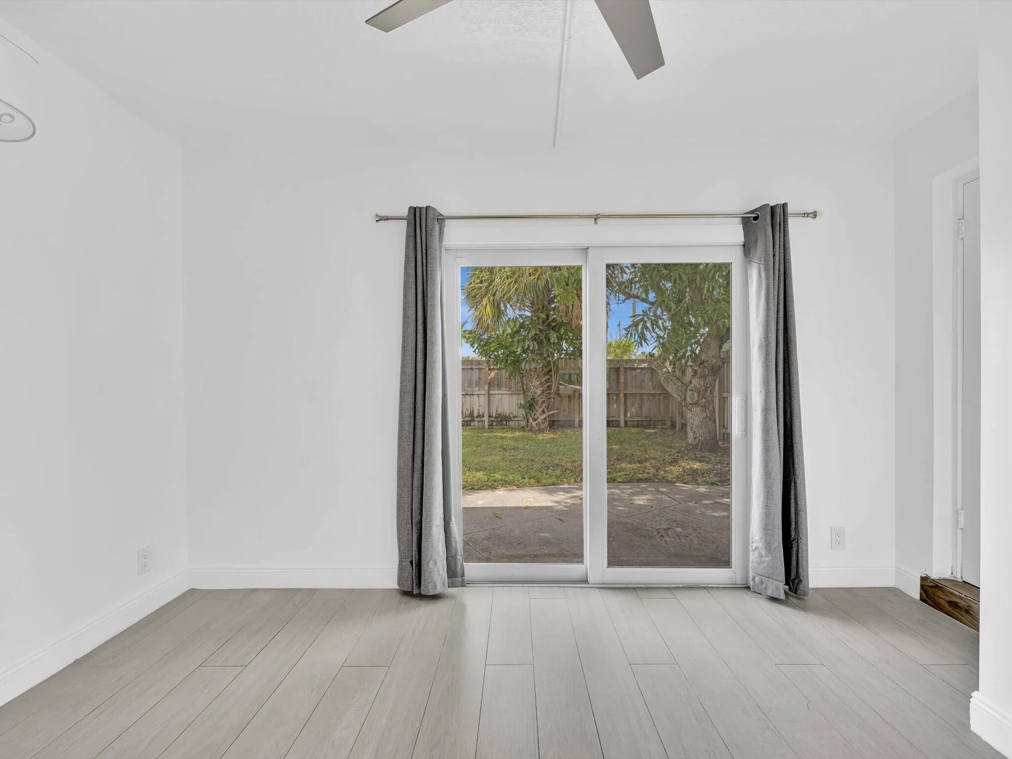 Bedroom with wood-finish ceiling fan with integrated lighting, and light grey vinyl flooring, sliding door exit to backyard