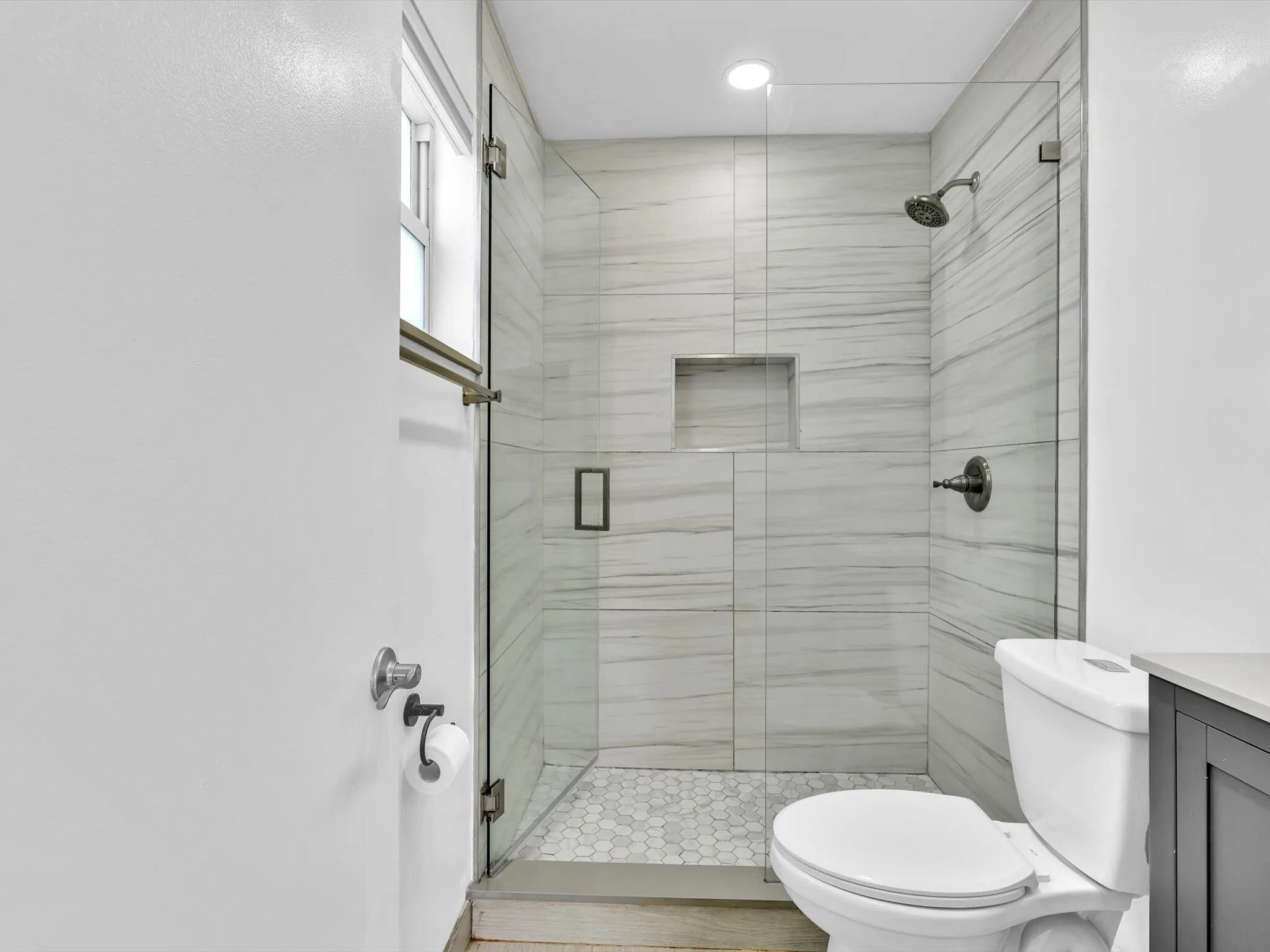 Primary Bedroom glass-enclosed shower with a recessed niche, hexagonal tile flooring, and horizontal tile walls