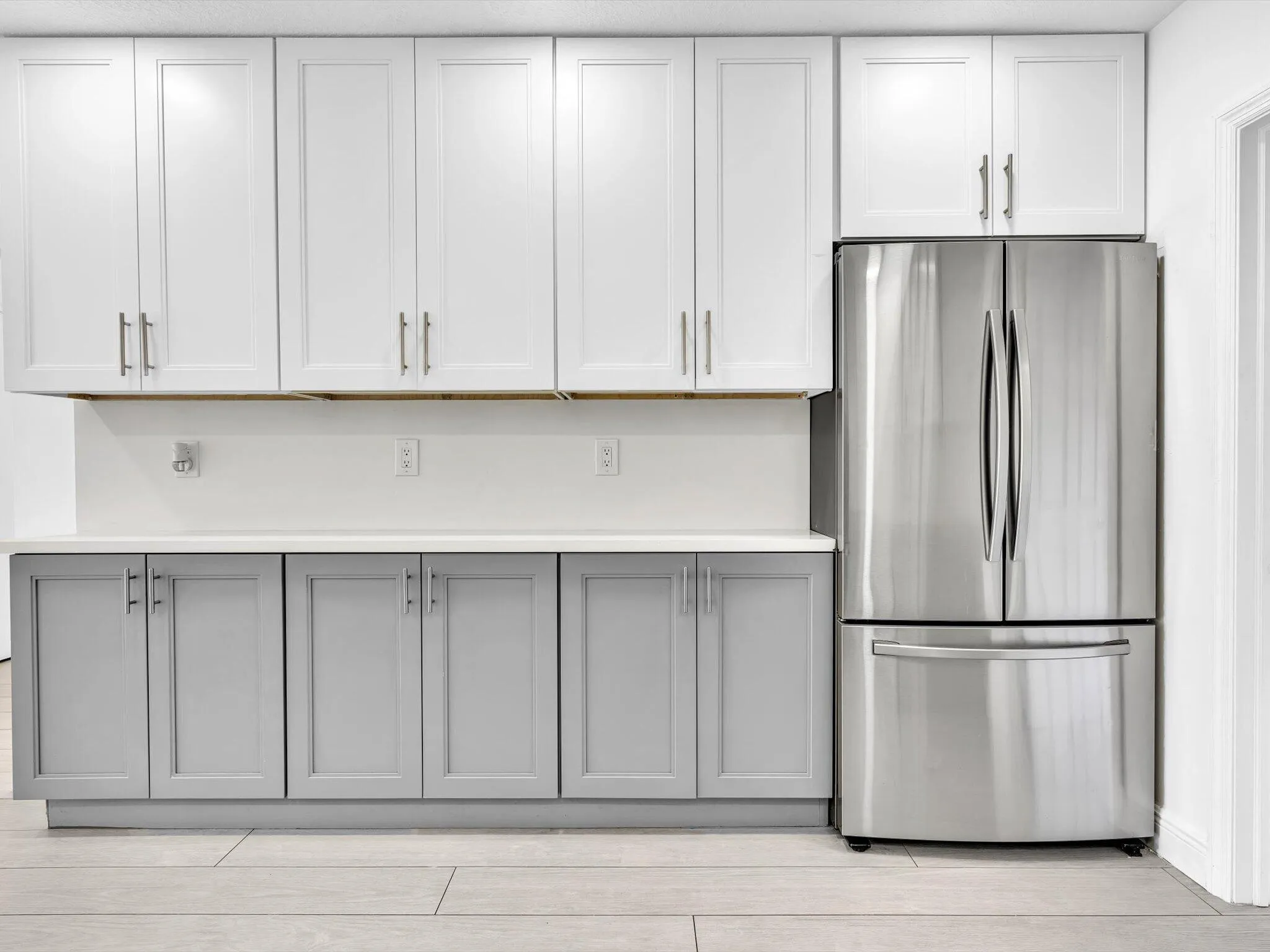 Kitchen featuring wood-finish vinyl flooring, two-tone cabinetry with white upper and grey lower units, stainless steel appliances, recessed lighting, and a white countertop