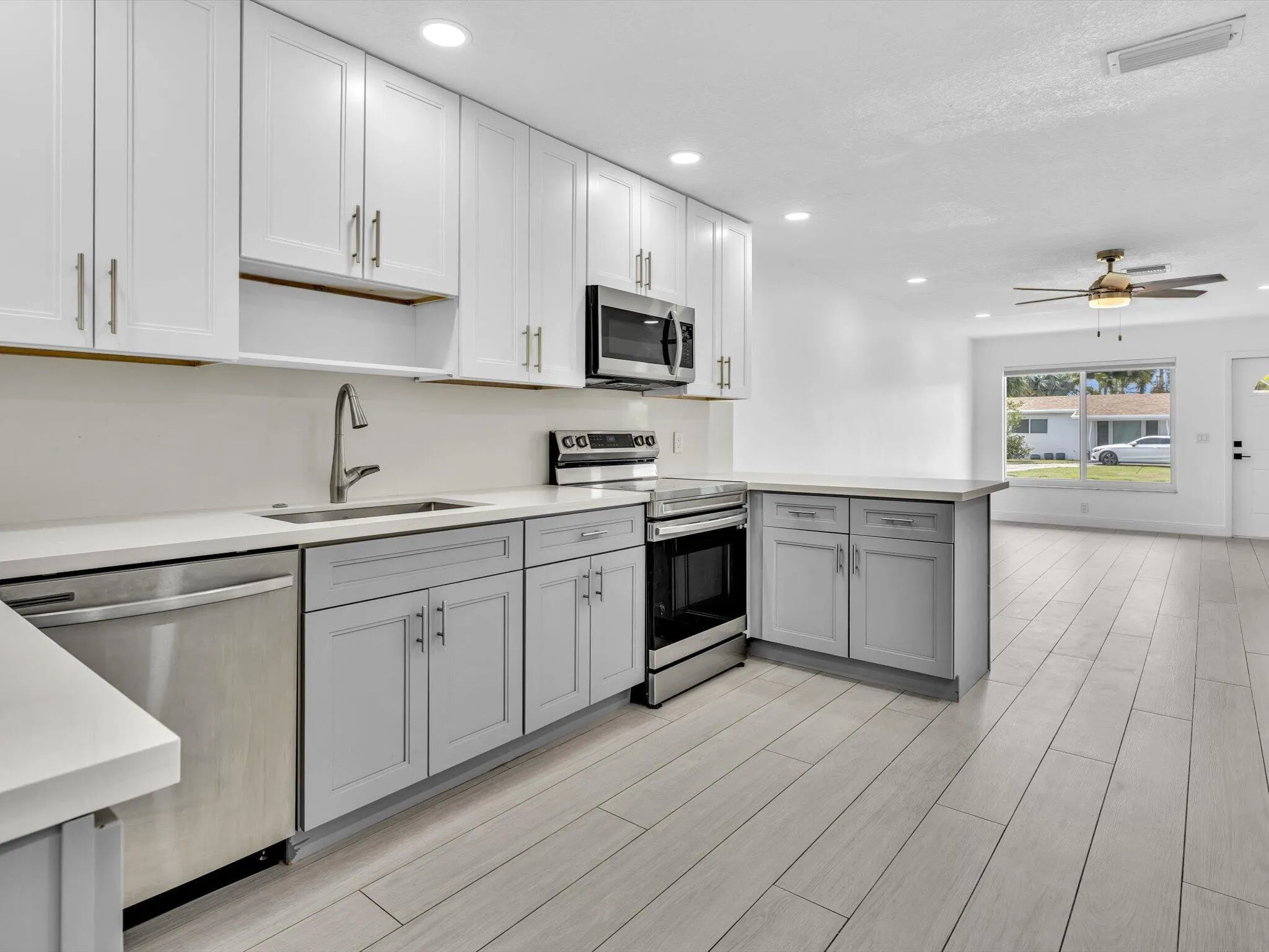 Kitchen featuring wood-finish vinyl flooring, two-tone cabinetry with white upper and grey lower units, stainless steel appliances, recessed lighting, and a white countertop