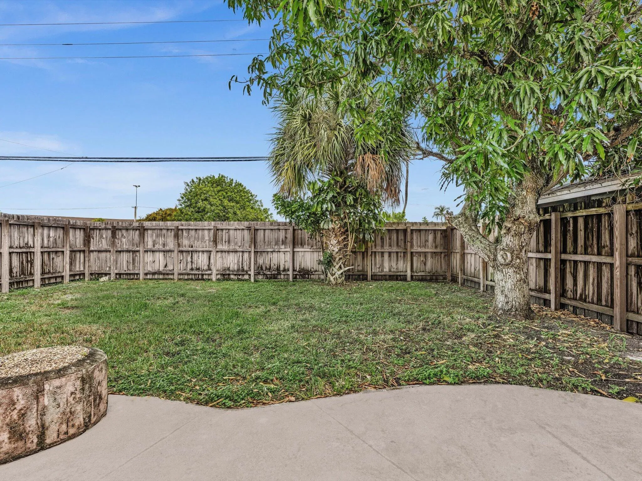 Private expansive fenced backyard featuring a concrete patio, wood fence, mature trees, and a grass lawn