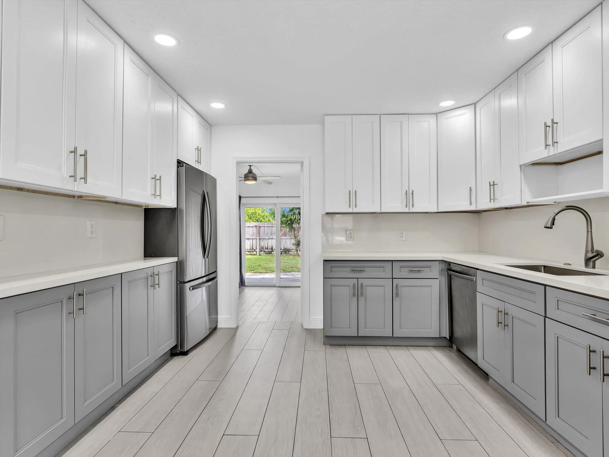 Kitchen featuring wood-finish vinyl flooring, two-tone cabinetry with white upper and grey lower units, stainless steel appliances, recessed lighting, and a white countertop