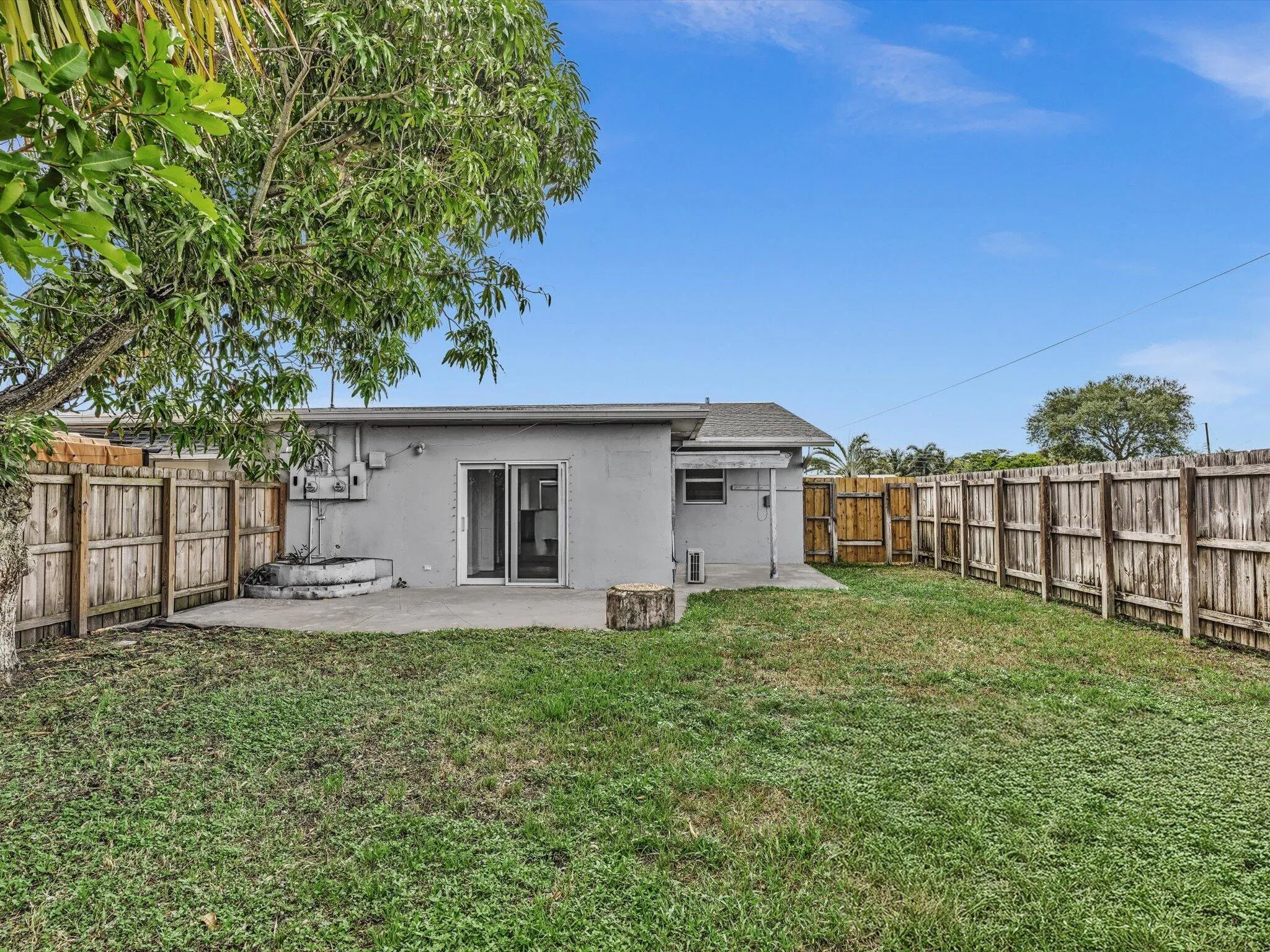 Private expansive fenced backyard featuring a concrete patio, wood fence, mature trees, and a grass lawn