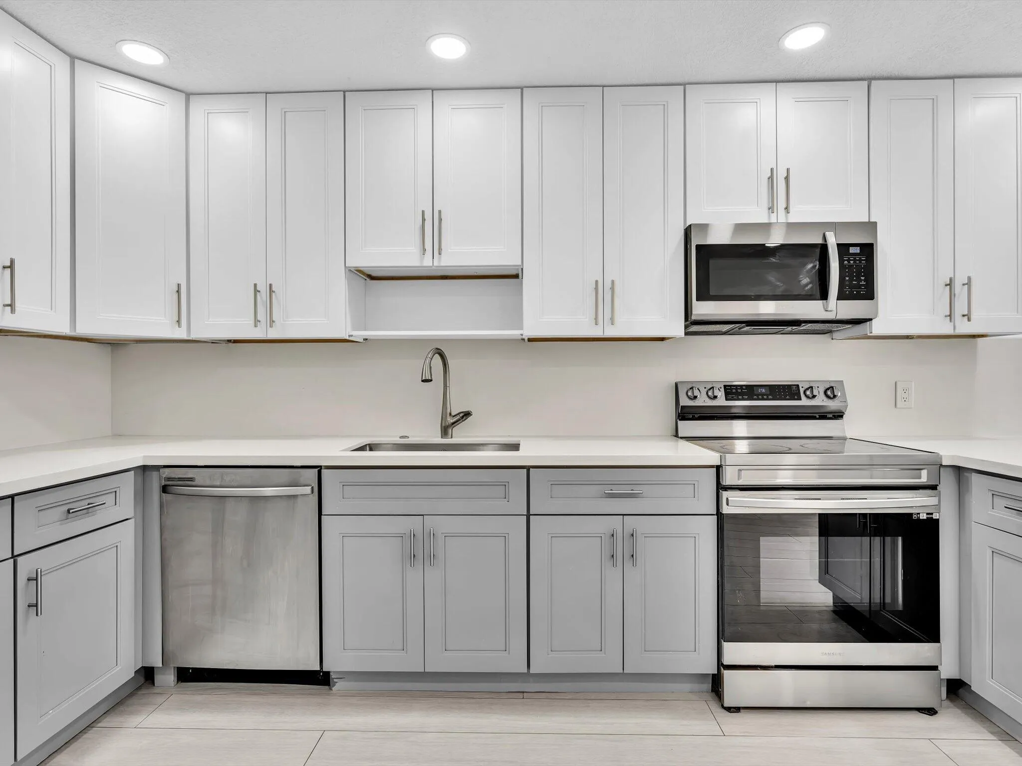 Kitchen featuring wood-finish vinyl flooring, two-tone cabinetry with white upper and grey lower units, stainless steel appliances, recessed lighting, and a white countertop