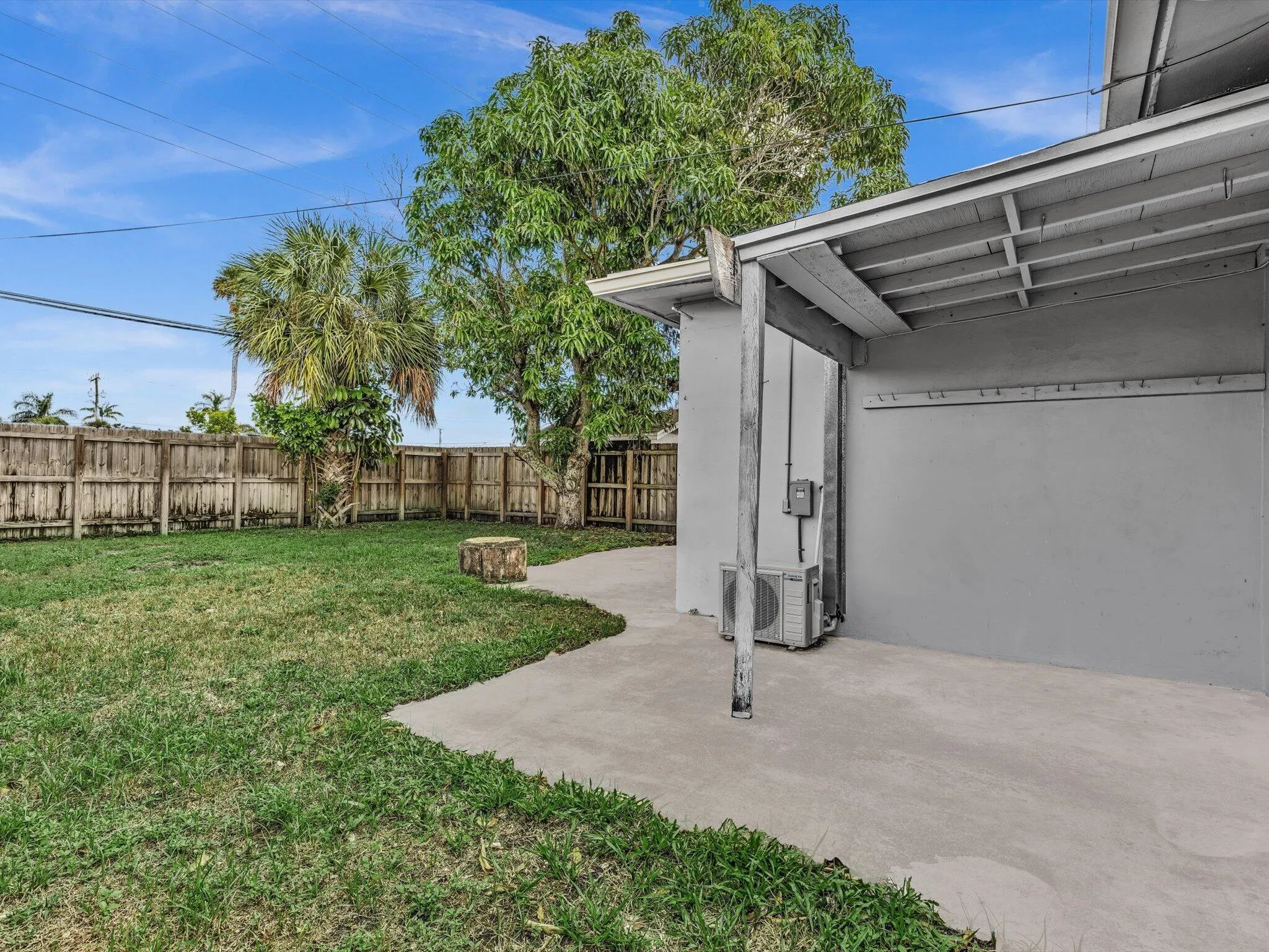 Private expansive fenced backyard featuring a concrete patio, wood fence, mature trees, and a grass lawn