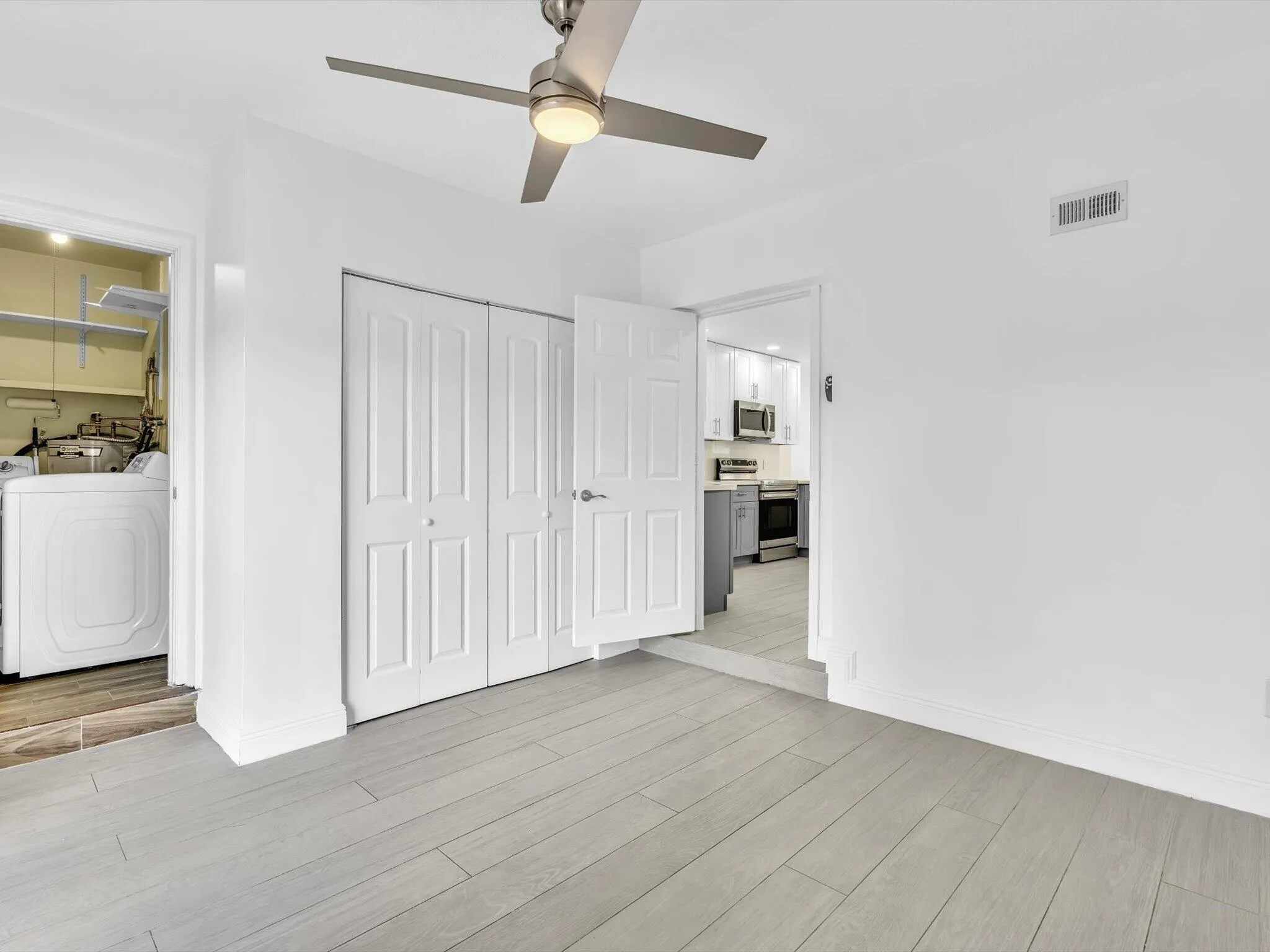 Bedroom with wood-finish ceiling fan with integrated lighting, and light grey vinyl flooring.