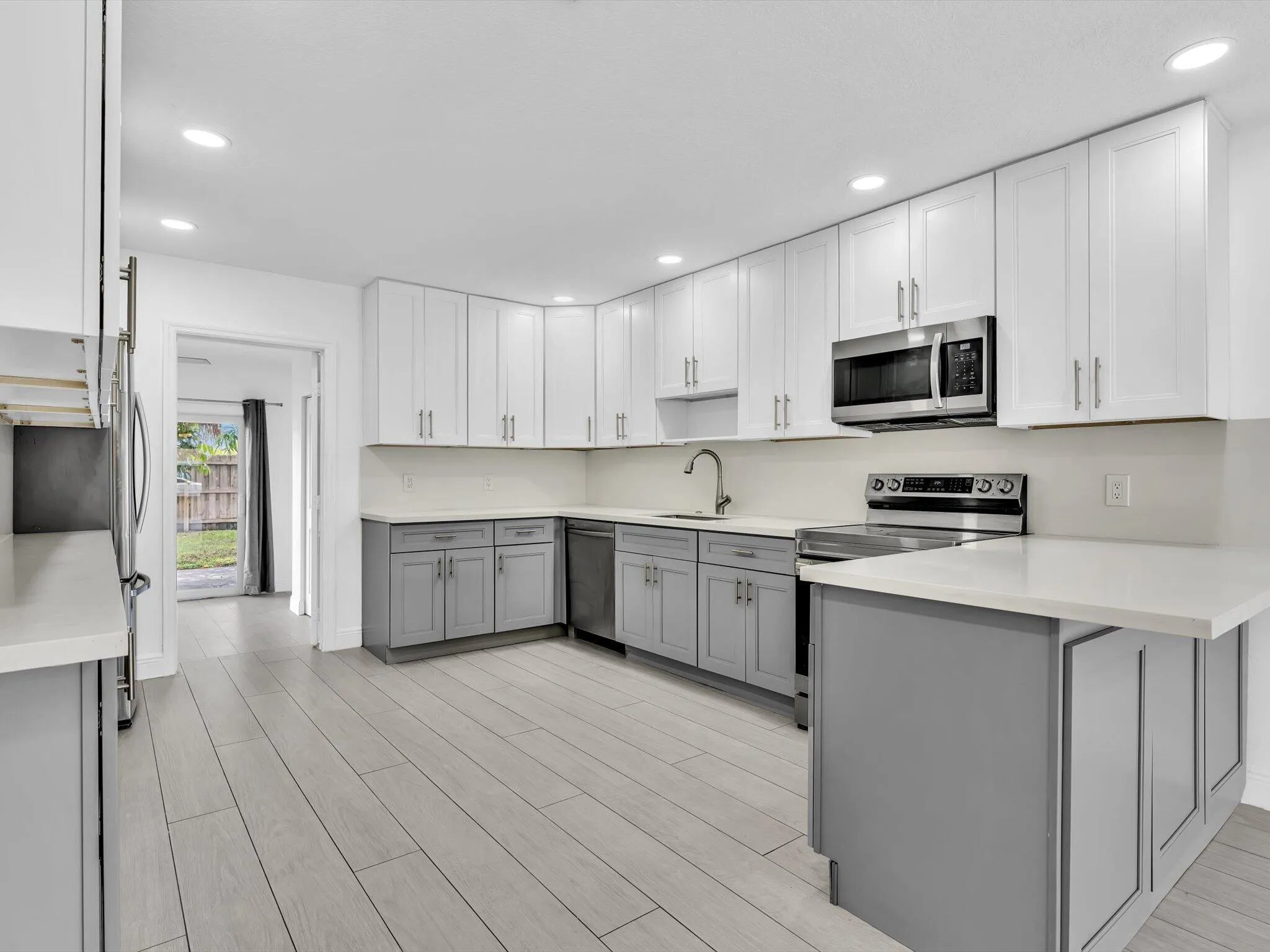 Kitchen featuring wood-finish vinyl flooring, two-tone cabinetry with white upper and grey lower units, stainless steel appliances, recessed lighting, and a white countertop