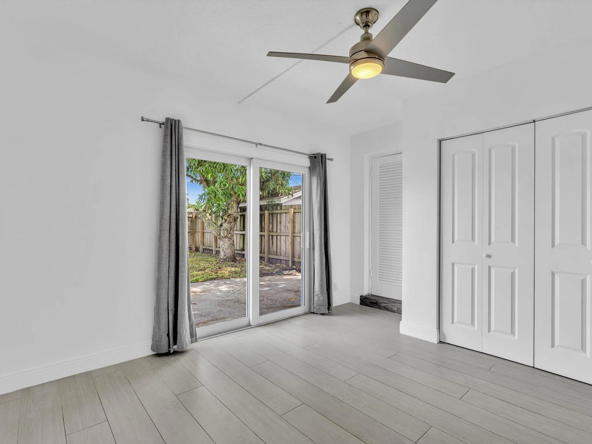Bedroom with wood-finish ceiling fan with integrated lighting, and light grey vinyl flooring, sliding door exit to backyard