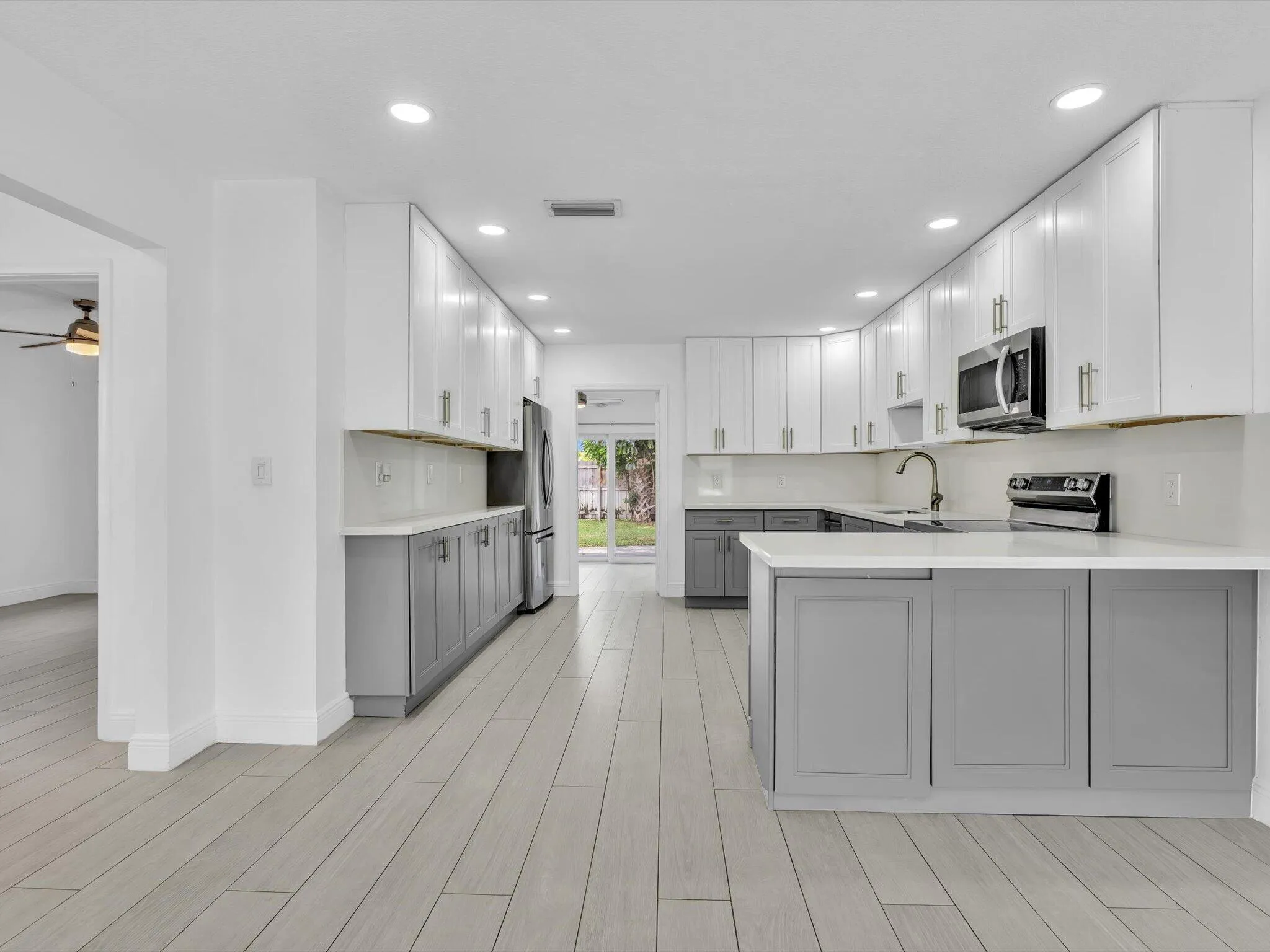 Kitchen featuring wood-finish vinyl flooring, two-tone cabinetry with white upper and grey lower units, stainless steel appliances, recessed lighting, and a white countertop