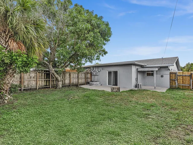 Private expansive fenced backyard featuring a concrete patio, wood fence, mature trees, and a grass lawn